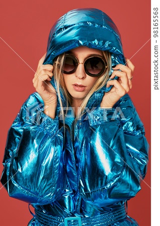 Blonde slim girl in blue down jacket covers her face from wind with hood 98165568