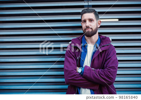 Handsome young man with hairstyle in fashionable clothes stands near iron wall and looking at the camera 98165840
