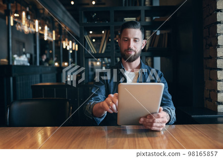 Modern hipster businessman drinking coffee in the city cafe during lunch time and working on tablet Modern hipster businessman drinking coffee in the city cafe during lunch time and working on tablet 98165857