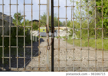 Old rusty iron gate on chain and lock. Closed metal gates. Protection, security and safety concept. padlock on metal gate closeup Old rusty iron gate on chain and lock. Closed metal gates. Protection, security and safety concept. padlock on metal gate closeup 98166715