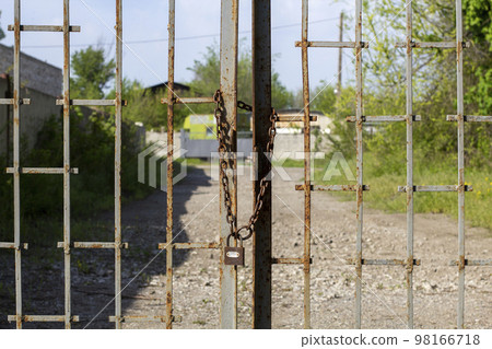 Old rusty iron gate on chain and lock. Closed metal gates. Protection, security and safety concept. padlock on metal gate closeup 98166718