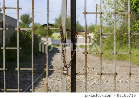 Old rusty iron gate on chain and lock. Closed metal gates. Protection, security and safety concept. padlock on metal gate closeup Old rusty iron gate on chain and lock. Closed metal gates. Protection, security and safety concept. padlock on metal gate closeup 98166719
