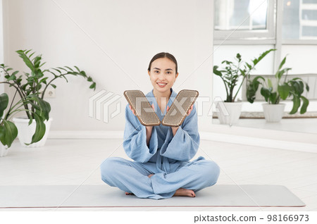 Asian woman sitting in lotus position on yoga mat and holding sadhu boards. Asian woman sitting in lotus position on yoga mat and holding sadhu boards. 98166973