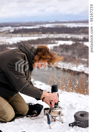 Male put small tourist kettle on fire in winter forest during camping, travelling 98167259