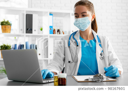 Young woman doctor sitting at working table using laptop Young woman doctor sitting at working table using laptop 98167601