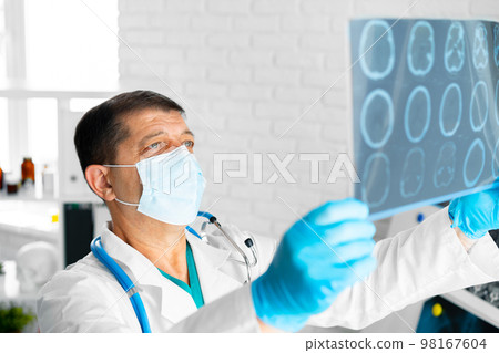 Senior man doctor in mask examines head MRI in hospital Senior man doctor in mask examines head MRI in hospital 98167604