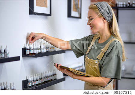 Perfumer taking notes of fragrances in assortment, essential aroma oils in bottles 98167815