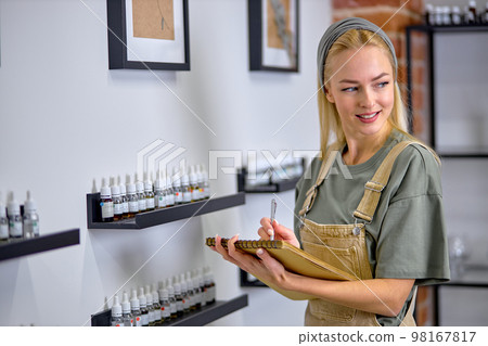 Perfume sample bottles in shelves. Woman take notes of fragrances, at work in shop 98167817