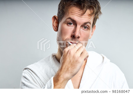 confused guy brushing tooth in early morning, after waking up. isolated on gray 98168047