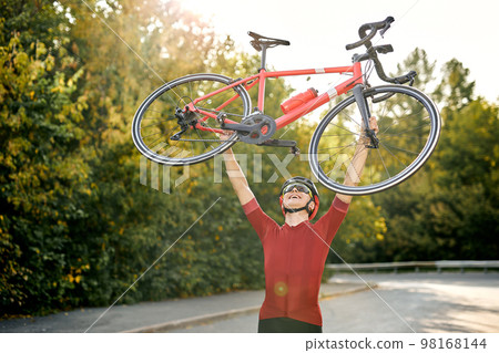Happy male in sportive clothes carrying raising bike up after successful competition Happy male in sportive clothes carrying raising bike up after successful competition 98168144