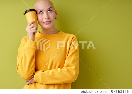 Portrait of thoughtful bald female holding cup of coffee in hands looking at side Portrait of thoughtful bald female holding cup of coffee in hands looking at side 98168316