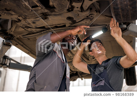 Young auto mechanics working on undercarriage of car diligence attention inspection 98168389
