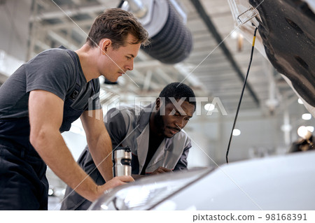 black and caucasian men can fix anything. car mechanics in uniform checking the engine black and caucasian men can fix anything. car mechanics in uniform checking the engine 98168391