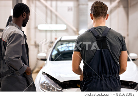 rear view on team of black and american guys looking under hood of broken car 98168392