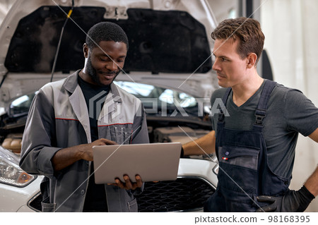 Handsome diverse mechanics in uniform examining car while working in workshop service 98168395