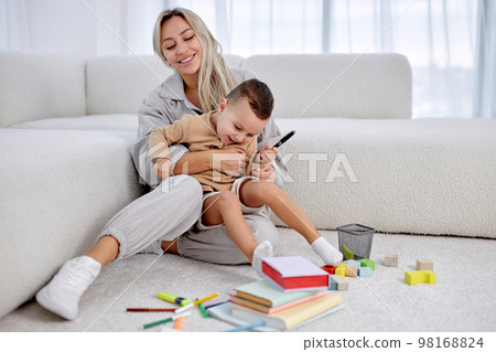 Positive young european mother play with excited smiling small son in living room Positive young european mother play with excited smiling small son in living room 98168824
