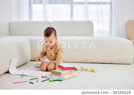 little boy draws on floor in bright living room. happy child draws with pencils. leisure. 98168826