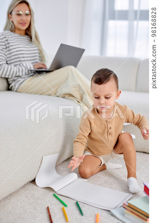 Kid boy and charming mother spending weekends at home together, child drawing on floor Kid boy and charming mother spending weekends at home together, child drawing on floor 98168828