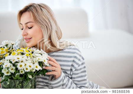 attractive female with wildflowers at home with a delicate smile on face. Blonde lady attractive female with wildflowers at home with a delicate smile on face. Blonde lady 98168836