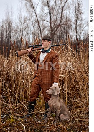 shikari with gray hunting dog in autumn forest. Image taken during big game hunting trip. shikari with gray hunting dog in autumn forest. Image taken during big game hunting trip. 98168975