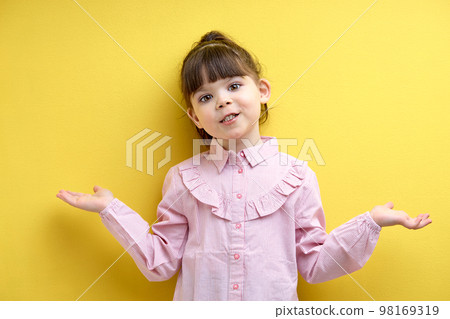 little girl with open hands asking sorry, isolated on yellow background. Oops. 98169319