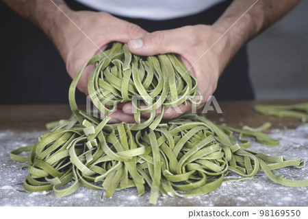 Fresh pasta. Homemade Italian raw pasta fettuccine with spinach in the hands of the chef on the background of the kitchen. 98169550