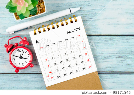 The April 2023 Monthly desk calendar for the organizer to plan 2023 year with alarm clock and pen on wooden table. 98171545