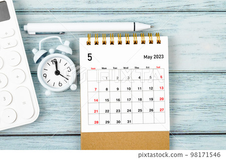 The May 2023 Monthly desk calendar for the organizer to plan 2023 year with alarm clock and calculator on wooden table. 98171546