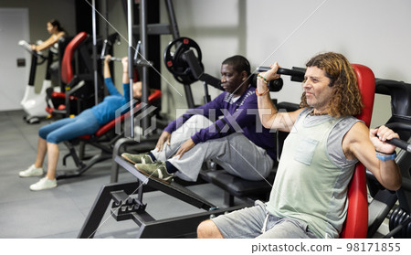 Caucasian man doing exercises on shoulder press machine in gym Caucasian man doing exercises on shoulder press machine in gym 98171855