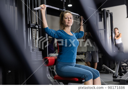 Caucasian woman doing exercises on lat pull down machine in gym 98171886