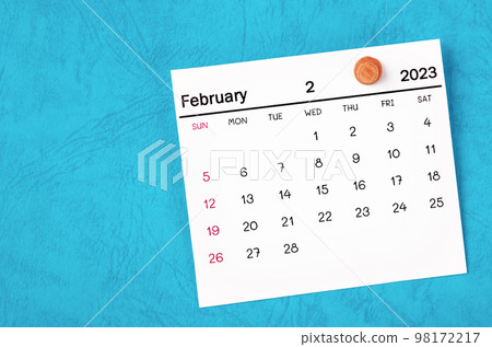 The February 2023 monthly calendar and wooden push pin on blue background. 98172217