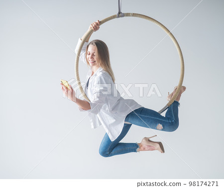 Caucasian female gymnast doing aerial hoop exercises and using smartphone.  98174271