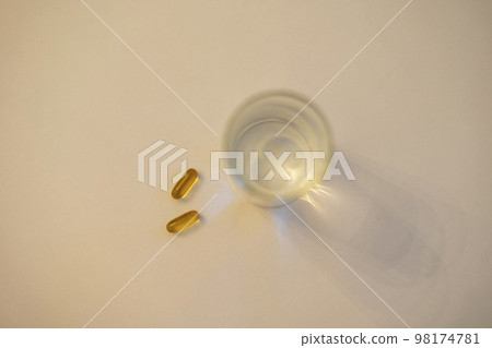 Pills and water cup lying on a white table Pills and water cup lying on a white table 98174781
