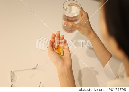 A woman's hand holding a glass of water with a pill in her hand, a woman's hand taking medicine A woman's hand holding a glass of water with a pill in her hand, a woman's hand taking medicine 98174798