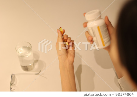 Woman holding pills in hand and looking at medicine cabinet, woman's hands taking pills Woman holding pills in hand and looking at medicine cabinet, woman's hands taking pills 98174804