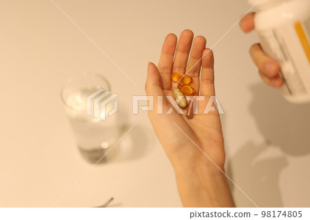 Woman putting medicine in hand and looking at medicine cabinet, woman's hand taking medicine Woman putting medicine in hand and looking at medicine cabinet, woman's hand taking medicine 98174805