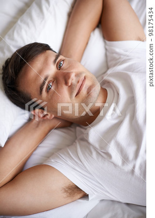 Enjoying some me-time. Portrait of a handsome young man lying in bed. Enjoying some me-time. Portrait of a handsome young man lying in bed. 98175434