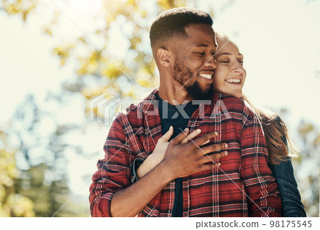 Diversity, love and couple hug in nature for relax summer holiday, outdoor freedom and happy quality time. African man, woman eyes closed and happiness together, hugging and loving in nature sunshine 98175545