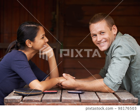 I am the luckiest guy on earth. A cute multi-racial couple sitting and holding hands while on a date. 98176503