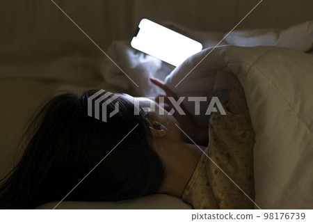 一個女人躺在床上,蓋著毯子,看著手機的後視圖 一個女人躺在床上,蓋著毯子,看著手機的後視圖 98176739