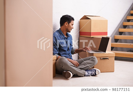 Moving day. A young man working on his laptop in between boxes. 98177151