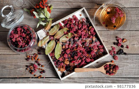 Wooden vintage background with a cup of fruit tea with dried berries of hawthorn, sea buckthorn, raspberries, plums, barberry and bird cherry. Wooden vintage background with a cup of fruit tea with dried berries of hawthorn, sea buckthorn, raspberries, plums, barberry and bird cherry. 98177836