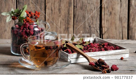 Wooden vintage background with a cup of fruit tea with dried berries of hawthorn, sea buckthorn, raspberries, plums, barberry and bird cherry. Wooden vintage background with a cup of fruit tea with dried berries of hawthorn, sea buckthorn, raspberries, plums, barberry and bird cherry. 98177837