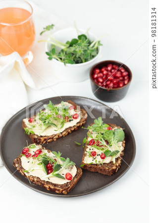 Sandwiches with soft cheese, microgreens, pomegranate seeds. Close-up on a white background, a glass of juice in the background. Sandwiches with soft cheese, microgreens, pomegranate seeds. Close-up on a white background, a glass of juice in the background. 98181314
