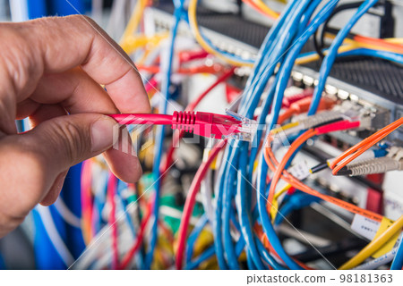 closeup of hand of administrator connecting network cable into switch 98181363