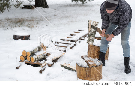 A man is chopping firewood with an axe in winter outdoor in the snow. Alternative heating, wood harvesting, energy crisis 98181904