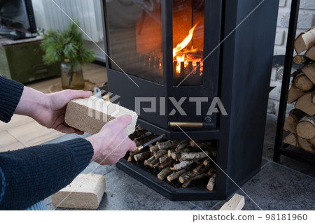 Hands kindle the hearth with economical briquettes. Fuel briquettes made of pressed sawdust for kindling the furnace - economical alternative eco-friendly fuel for the fireplace in the house. 98181960