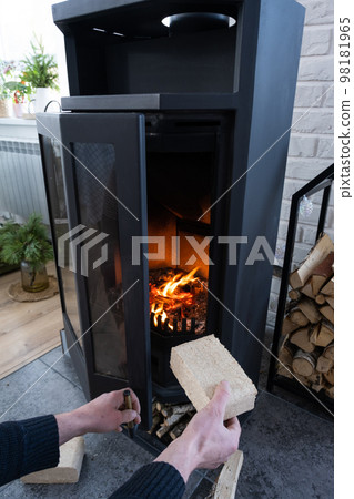 Hands kindle the hearth with economical briquettes. Fuel briquettes made of pressed sawdust for kindling the furnace - economical alternative eco-friendly fuel for the fireplace in the house. 98181965