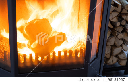 Fuel briquettes made of pressed sawdust for kindling the furnace - economical alternative eco-friendly fuel for the fireplace in the house. Firewood is burning in the oven in the interior Fuel briquettes made of pressed sawdust for kindling the furnace - economical alternative eco-friendly fuel for the fireplace in the house. Firewood is burning in the oven in the interior 98181967
