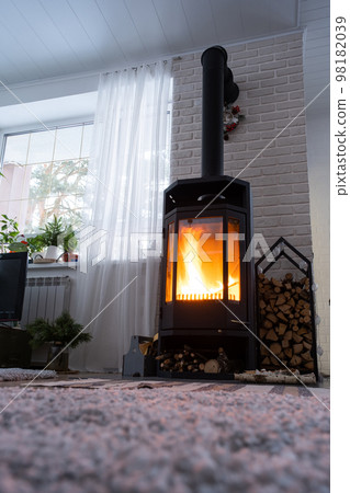 Black stove, fireplace in interior of house in loft style. Alternative eco-friendly heating, warm cozy room at home, burning wood Black stove, fireplace in interior of house in loft style. Alternative eco-friendly heating, warm cozy room at home, burning wood 98182039